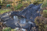 Pond protected against falling leaves and winter weather with black tarpaulin in backyard garden in autumn, Quebec, Canada. 