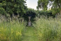 View of urn with wild grasses framing.  Medlar tree, Mespilus germanica, to the left. 