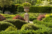 A carved stone urn surrounded by mixed topiary of Taxus baccata and Berberis in the walled garden demonstating alternative planting to Box at RHS Wisley