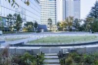 Main  plaza with view to surrounding skyscrapers. Circular terrace of paved, grass and concrete surfaces with surrounding rill. 