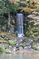 Waterfall splashing onto rocks with trees with autumn colour. 