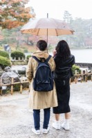 Two women visitors sheltering under umbrella from rain, which is showing as streaks on the womans hair and clothes on right. 