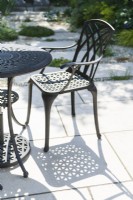 Aluminium alloy garden table and chair casting shadows on limestone paving in summer. June.