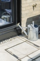 Close-up of drainage inspection cover with inset limestone paving next to patio doors. Outside tap with galvanised watering can. June