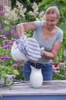 Making nettle fertiliser and insecticide. Woman filtering mixture of water and nettles through the kitchen cloth into an enamel jug.