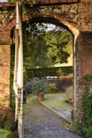View through a gate into a formal garden with pots of salvias and squashes drying on a low wall in October