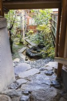 View from steps to upper floor of house onto a small courtyard with granite pebbles and narrow stone slab path with stone on path tied with string to indicate no entry. This is called Tome ishi. Water feature with small pool.