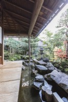 Covered veranda at the back of the house with view into the garden. Rocks placed as stepping stones across water with two stone lanterns or Ishidoro. 