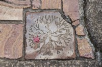Detail of decorative tile in path with leaf of Acer.