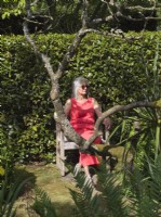 Mature woman relaxing on rustic wooden chair in secluded garden area