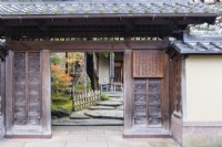 View into the entrance to the house and garden with notices in Japanese and wide stepping stones inside entrance and a low bamboo railing.