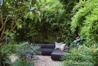 Corner sofa on gravel area in secluded part of garden. Planting includes Mahonia Soft Caress, Eriobotrya japonica and Bamboo