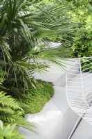 White paving, steps and chair next to raised bed with lush planting