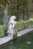 An old lion sculpture spouts water into a pool in the Real Alcazar Palace gardens, Seville. Spain. September. 