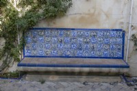 A colourful, Moorish style, tiled bench within the Jardins de las Flores, Garden of Flowers, with a brick path in front. Real Alcazar Palace gardens, Seville. Spain. September. 