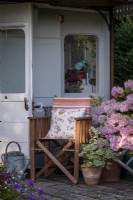 Old fashioned vintage garden chair surrounded with containers filled with summer flowers