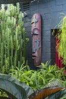 Corner of a lush subtropical garden featuring a Philodendron, 'Rojas', Euphorbia trigona and a carved tribal mask.