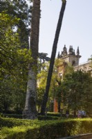  A view across clipped hedges and a variety of foliage to an ornate facade at the Royal Alcazar Palace gardens, Seville. Spain. September. 