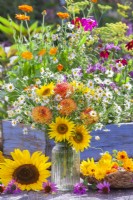 Yellow-orange-white summer flower bouquet in a glass vase containing Sunflowers, Dahlia and Chamomille.