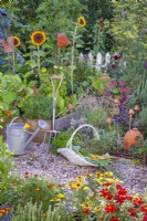 A basket of picked vegetables in front of a bed of mixed herbs and raised beds full of growing vegetables and annual flowers.