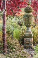 Terracotta urn surrounded by shrubs, ornamental grasses and trees including Prunus serrula in November