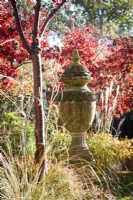 Terracotta urn surrounded by colourful trees and shrubs and ornamental grasses in November
