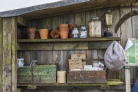 Wooden old boxes with old gardening books, packets of seeds and clay pots, garden twine and jars stand on shelves in a wooden shed