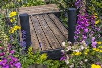 Charred wooden boardwalk set among flowering perennials. June
