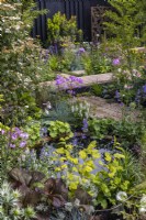 Perennial bed with a corten water bowl. Wooden and gravel boardwalks lead among flowering perennials and shrubs. June,  Designer: Robert Moore 