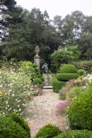 A view through The Flower Garden towards the pond and fountain with a gravel path, perennials and box topiary.