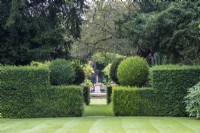 Clipped yew hedges frame a view through to a statue at The Manor, Little Compton, Cotswolds.