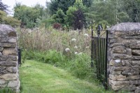 A dry stone wall and iron gate lead into the wildflower meadow at The Manor, Little Compton.