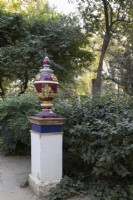 A brightly coloured urn stands on top of a column amongst a variety of foliage. Parque de Maria Luisa, Seville, Spain. September