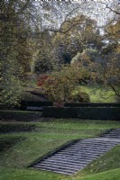 View across the 'tilt yard' with grass terraces and a flight of stone steps in autumn at Dartington Hall, Devon