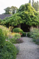 A gravel path leads past topiary and flowerbeds to a wisteria-covered summer house in the Flower Garden at The Manor, Little Compton.