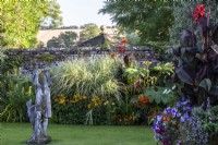 The summer borders and a statue in the Swimming Pool Garden at The Manor, Little Compton. Planting includes Miscanthus sinensis 'Variegatus', Canna 'Roi Humbert' and Tetrapanex 'Rex'.