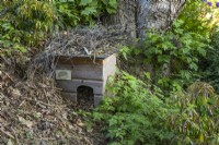 Wooden hedgehog house camouflaged with twigs in a woodland garden
