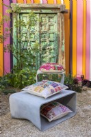 Stool and table made of cement fibre with coloured cushions. Angelica archangelica and green old wooden door in the background. Designer: Manoj Malde
