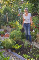 A woman plans to plant a bed of annuals including Tagetes patula and Calendula officinalis next to a vegetable bed.