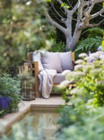 Secluded seating area with armchair and lanterns surrounded by Melanoselinum decipiens and architectural fig Ficus carica. Hamptons Mediterranean Garden, Designer: Filippo Dester Garden Club London, RHS Chelsea Flower Show 2023