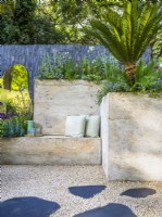 Inbuilt seating made from hypertufa, resembling natural stone by raised bed with Alliums and Cycas revoluta. The Shifting Garden, Designer: The Chelsea Gardener, RHS Chelsea Flower Show 2023