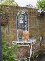 Wrought iron table and mirror against brick wall in cottage garden