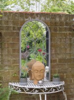Wrought iron table and mirror against brick wall in cottage garden