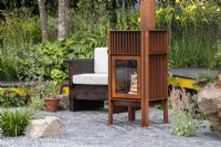 A seating area with chair and metal outdoor wood burning stove set on reclaimed granite setts Hurtigruten: The Relation-Ship Garden, Max Parker-Smith, RHS Hampton Court Palace Garden Festival