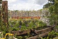 A sustainable garden with raised pools made from reclaimed sleepers, and a boundary wall made of gabions filled with stone offcuts. Pollinator friendly planting includes achillea and echinacea  - Caroline and Peter Clayton - Get Started Gardens - Nurturing Nature in the City, RHS Hampton Court Palace Garden Festival.