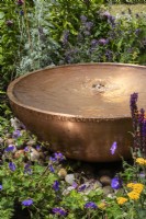 Circular copper water feature with bubble fountain. Planting includes Geranium 'Rozanne' and achillea. Designer Penelope Hill Smith - The Wilton London Botanical Fragrance Garden - RHS Hampton Court Palace Garden Festival.