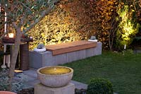 Light in the garden, illuminated beech hedge with bench in front 