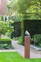 Formal garden with yew hedges and bird sculpture on a plinth, Chinese hardstone and brick paving 