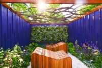 Relaxation area surrounded by a navy blue painted panels with decorative wooden deckchairs set against living green wall under with geometric design openwork of pergola roof. June
Bord Bia Bloom, Dublin
Designer: Jane McCorkell


