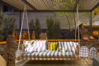 A sitting area on a gravel surface surrounded by a low stone fence with a wooden swing with pillows among luminescent decorative lamps in Luxurious African lodge.
Designer: Vetschpartner, Berger Gartenbau and Livingdreams. Giardina-Zurich, Swiss.





